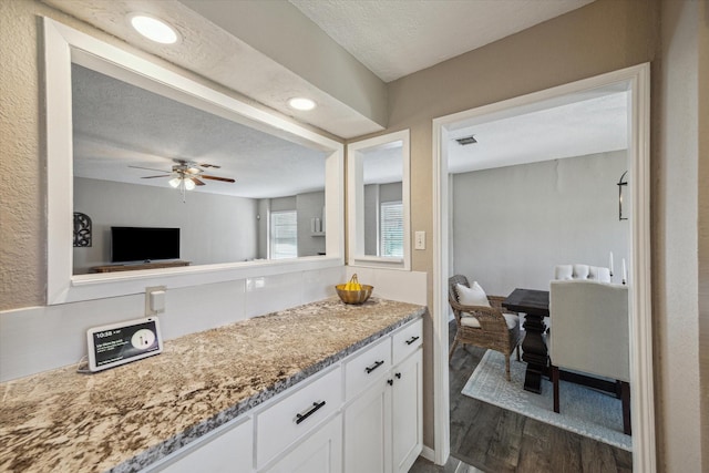 kitchen with a ceiling fan, light stone counters, a textured ceiling, dark wood-style floors, and white cabinets