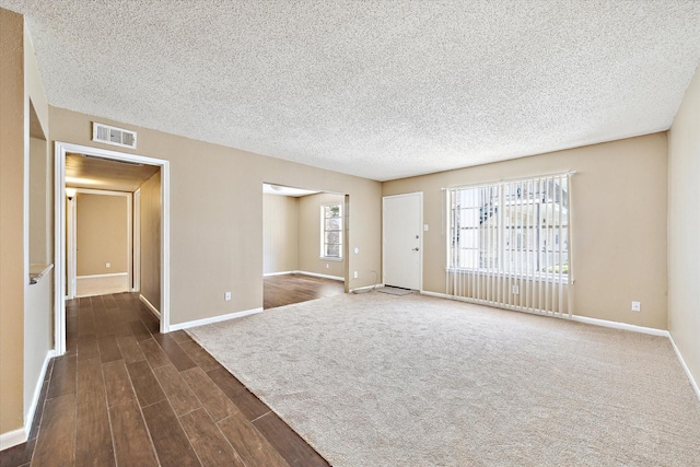 spare room featuring baseboards, dark wood-style floors, visible vents, and a textured ceiling