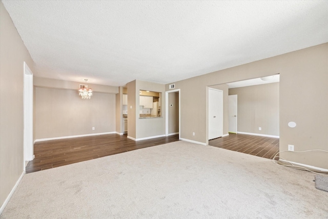 unfurnished living room with an inviting chandelier, visible vents, dark colored carpet, and a textured ceiling