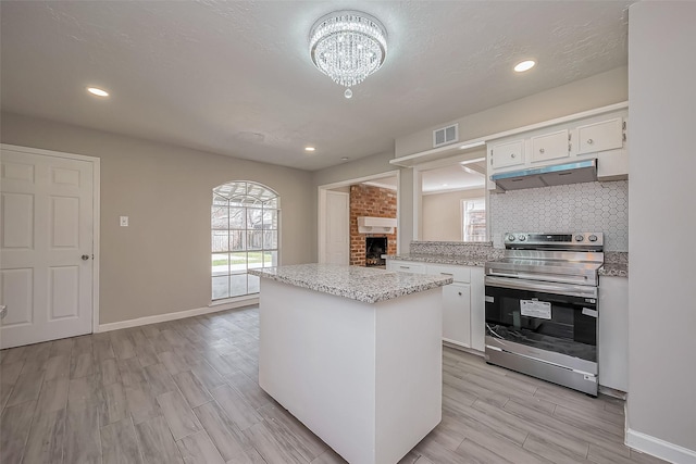 kitchen with under cabinet range hood, backsplash, white cabinets, and stainless steel electric range oven