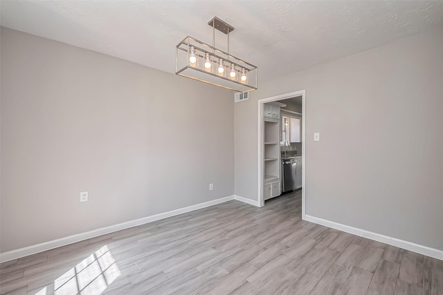 unfurnished dining area with visible vents, baseboards, wood finished floors, a textured ceiling, and a sink