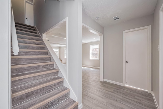 staircase with a textured ceiling, wood finished floors, visible vents, and baseboards