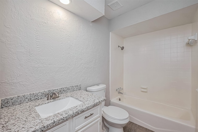 bathroom featuring vanity, visible vents, shower / bath combination, toilet, and a textured wall