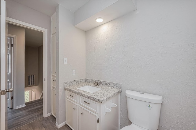 bathroom featuring visible vents, toilet, wood finished floors, vanity, and a textured wall