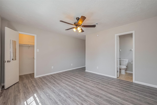 unfurnished bedroom with baseboards, a textured ceiling, wood finished floors, and a spacious closet