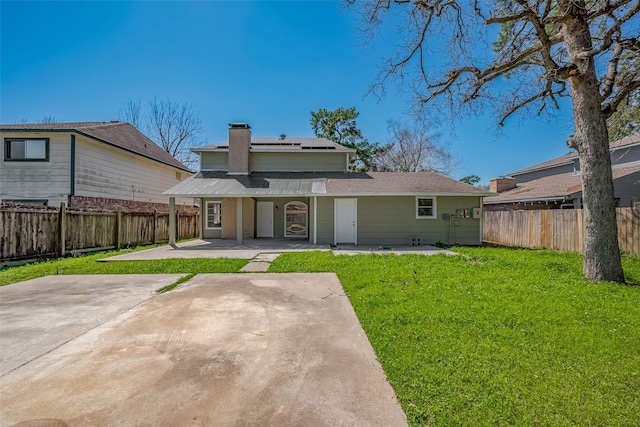 back of house featuring a fenced backyard, roof mounted solar panels, a patio, and a yard