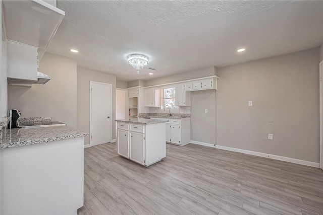 kitchen with tasteful backsplash, baseboards, light wood-style flooring, white cabinetry, and a sink