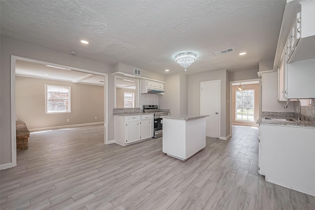 kitchen featuring stainless steel range with electric stovetop, a sink, plenty of natural light, backsplash, and a kitchen island