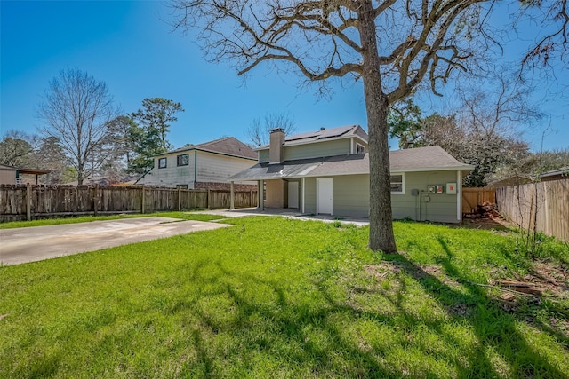 rear view of house featuring a lawn, a patio, a fenced backyard, solar panels, and a chimney