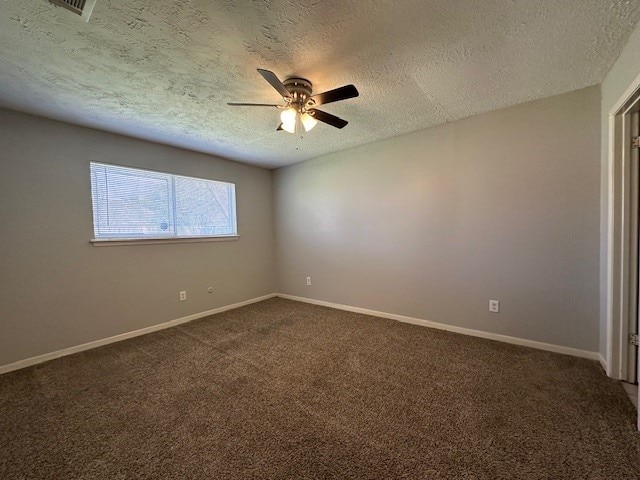 empty room featuring baseboards, a ceiling fan, dark carpet, and a textured ceiling