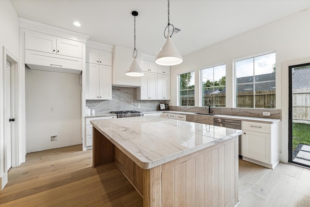 kitchen featuring tasteful backsplash, a kitchen island, light wood-type flooring, white cabinets, and a sink