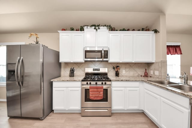 kitchen with a sink, stainless steel appliances, backsplash, and white cabinetry