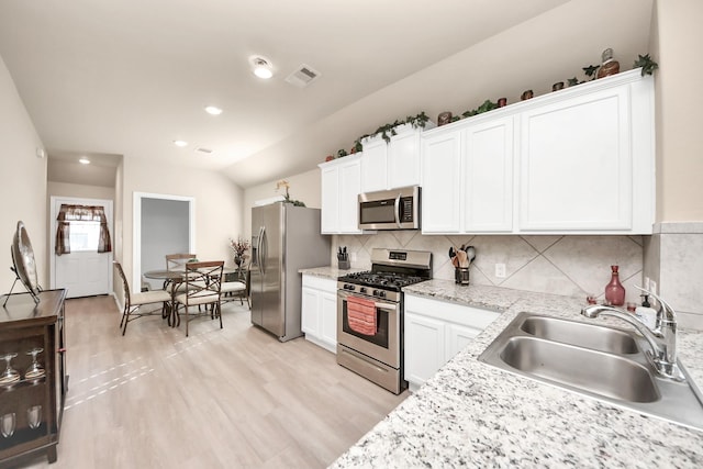 kitchen with visible vents, a sink, stainless steel appliances, vaulted ceiling, and white cabinets