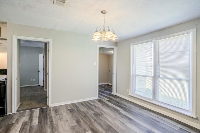 unfurnished dining area with visible vents, baseboards, wood finished floors, a notable chandelier, and a textured ceiling