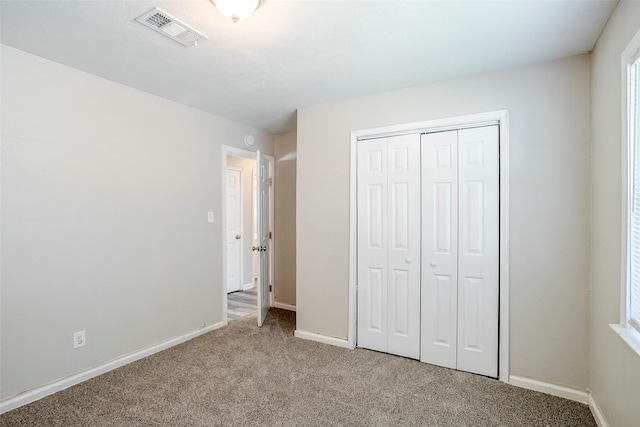 unfurnished bedroom with baseboards, visible vents, a closet, and light carpet