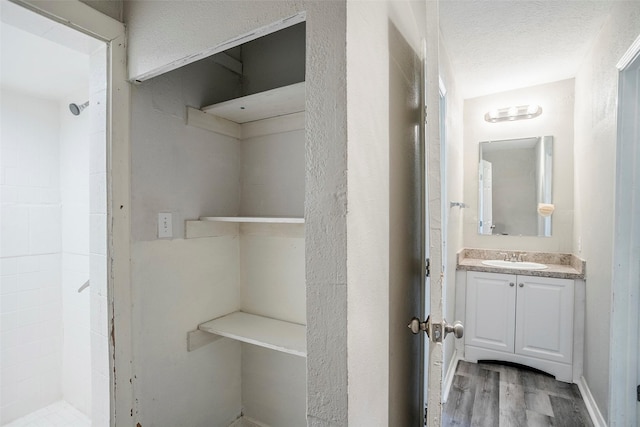 full bathroom with vanity, wood finished floors, a tile shower, and a textured ceiling