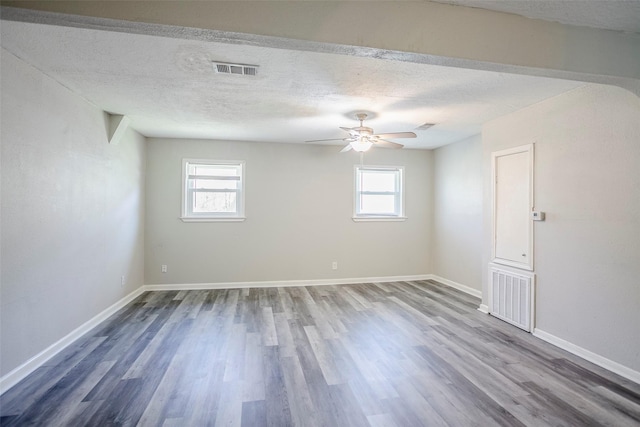 empty room featuring wood finished floors, visible vents, a wealth of natural light, and a textured ceiling