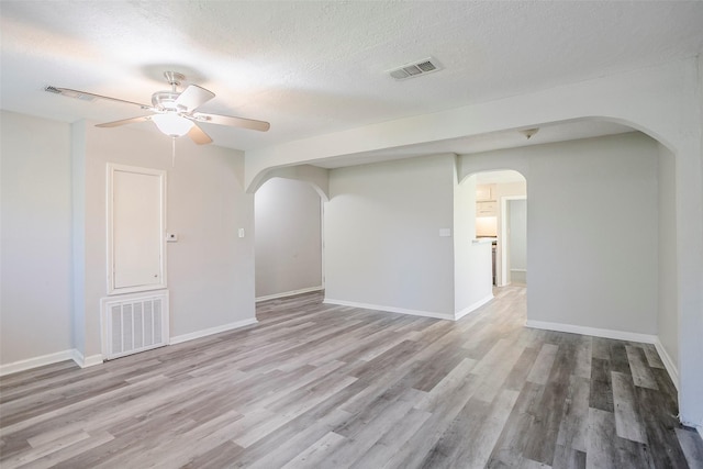 empty room featuring a ceiling fan, wood finished floors, arched walkways, and visible vents