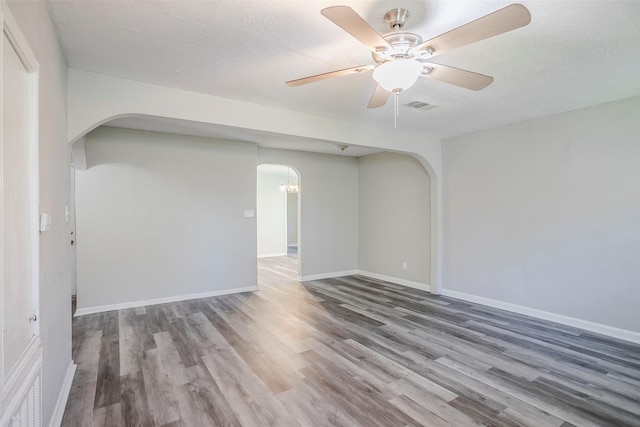 unfurnished room featuring arched walkways, wood finished floors, and a ceiling fan