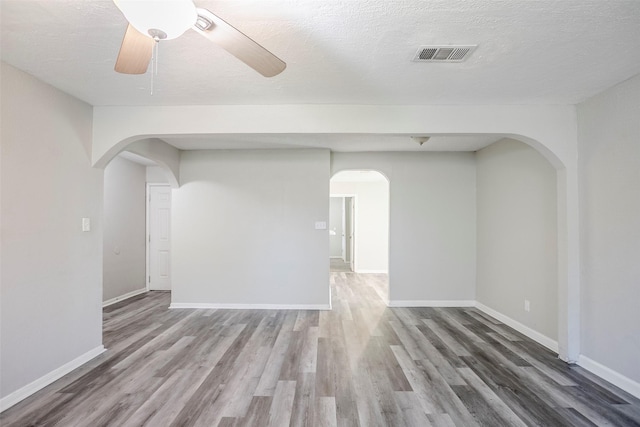 empty room with visible vents, baseboards, wood finished floors, arched walkways, and a textured ceiling