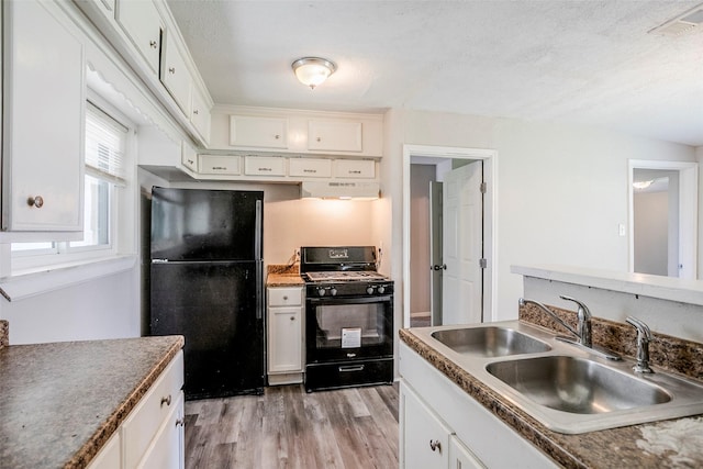 kitchen with a sink, black appliances, light wood-style floors, under cabinet range hood, and white cabinetry