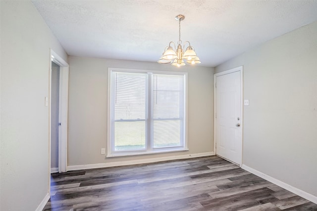 unfurnished dining area with baseboards, a textured ceiling, an inviting chandelier, and wood finished floors