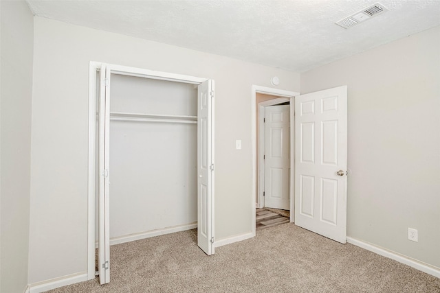 unfurnished bedroom with baseboards, visible vents, a closet, a textured ceiling, and light carpet