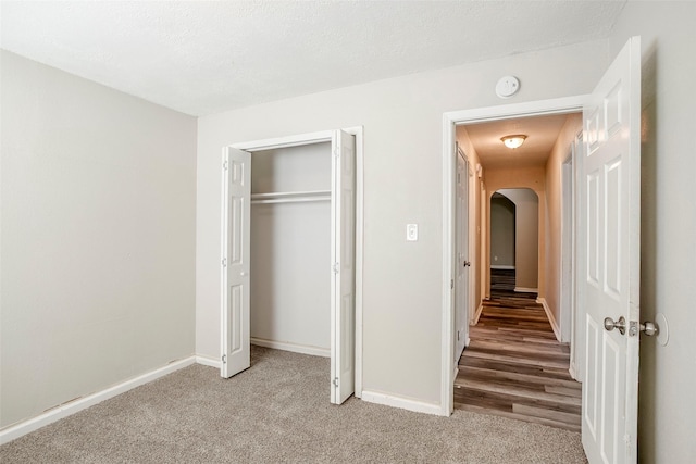 unfurnished bedroom with arched walkways, a closet, baseboards, and carpet