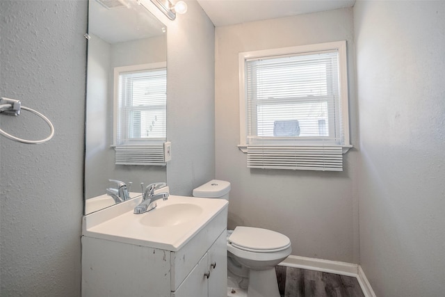 half bath featuring visible vents, baseboards, toilet, wood finished floors, and vanity