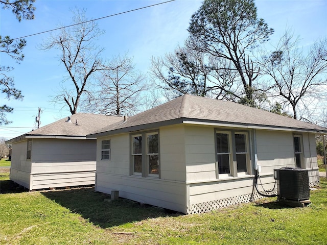 view of property exterior with a yard, central AC, and a shingled roof