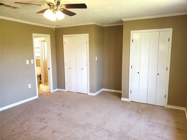 unfurnished bedroom with visible vents, two closets, carpet, and ornamental molding