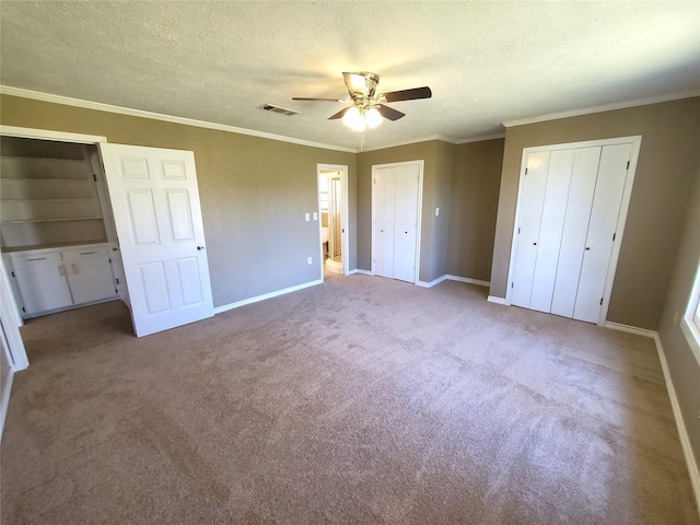 unfurnished bedroom featuring multiple closets, ornamental molding, a textured ceiling, carpet flooring, and baseboards