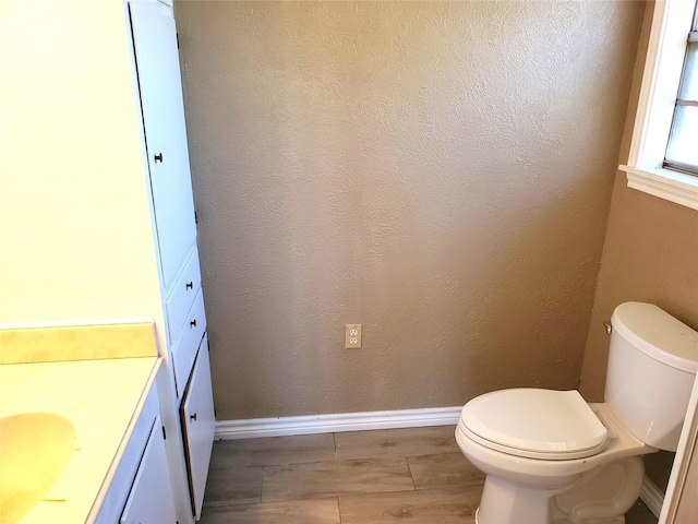 bathroom featuring toilet, wood tiled floor, baseboards, vanity, and a textured wall