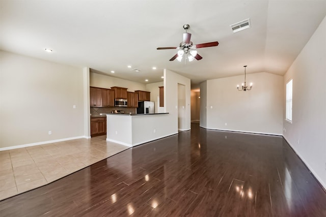 unfurnished living room featuring visible vents, baseboards, lofted ceiling, ceiling fan with notable chandelier, and wood finished floors