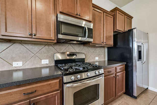 kitchen featuring brown cabinetry, baseboards, light tile patterned flooring, appliances with stainless steel finishes, and backsplash