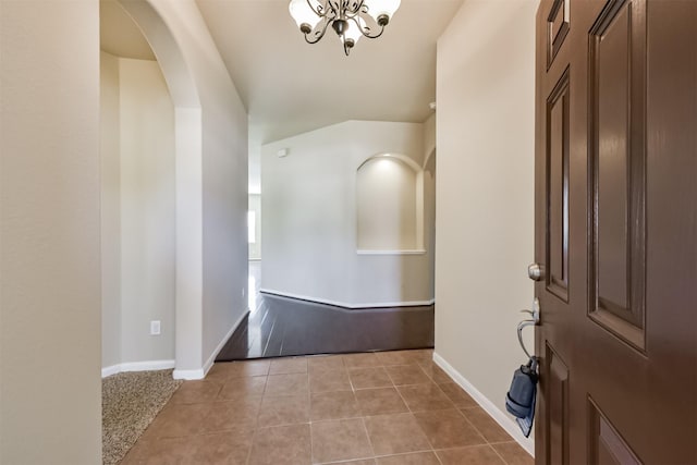 entryway with light tile patterned floors, a chandelier, arched walkways, and baseboards