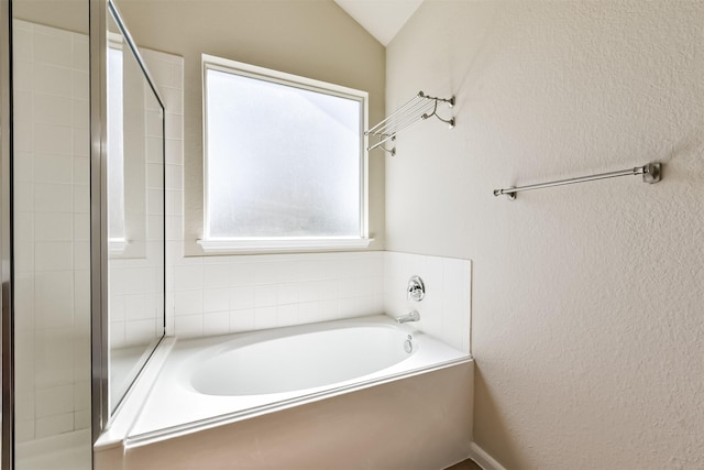 bathroom featuring a bath, a shower stall, and a textured wall