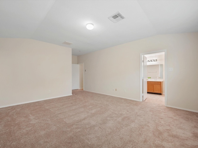 spare room with visible vents, baseboards, light colored carpet, and vaulted ceiling