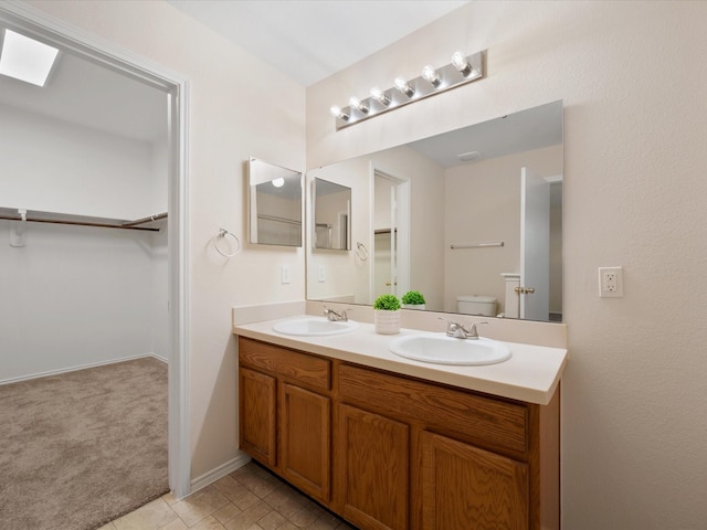 bathroom with a walk in closet, double vanity, toilet, and a sink