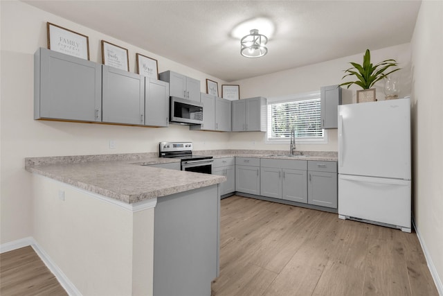 kitchen with gray cabinetry, appliances with stainless steel finishes, a peninsula, light wood-style floors, and a sink