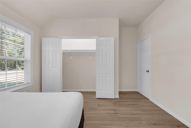 bedroom with a closet, baseboards, vaulted ceiling, and light wood finished floors