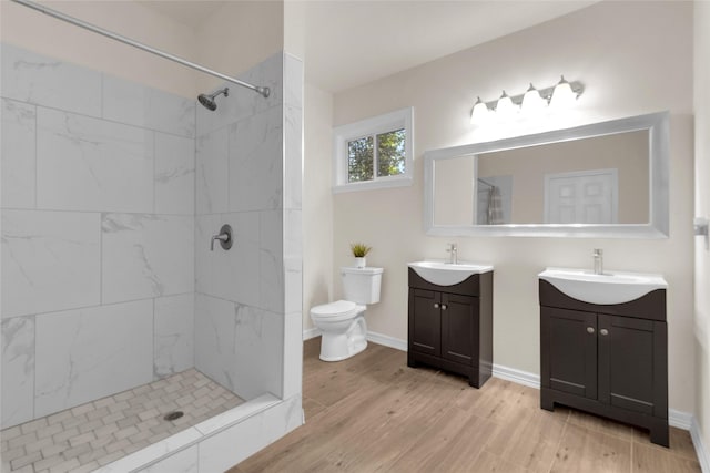 full bathroom featuring wood finished floors, baseboards, tiled shower, two vanities, and toilet