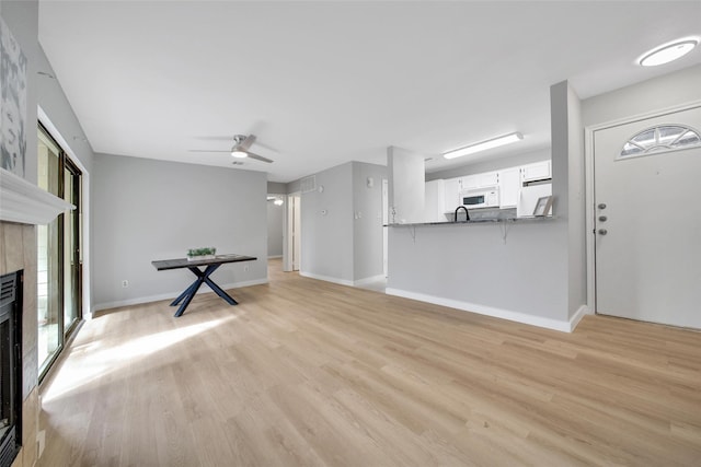 unfurnished living room with light wood-type flooring, baseboards, ceiling fan, and a tile fireplace