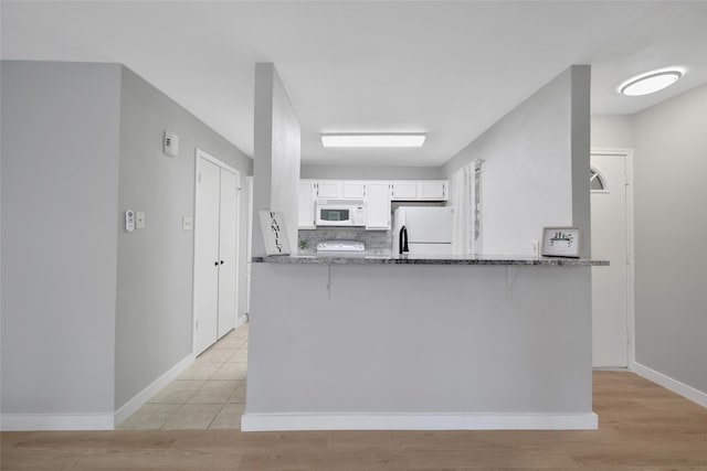 kitchen featuring white appliances, dark stone countertops, a kitchen bar, white cabinetry, and backsplash