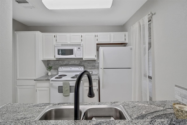 kitchen with white appliances, white cabinets, visible vents, and a sink