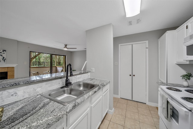 kitchen with white appliances, visible vents, a tile fireplace, a sink, and white cabinets