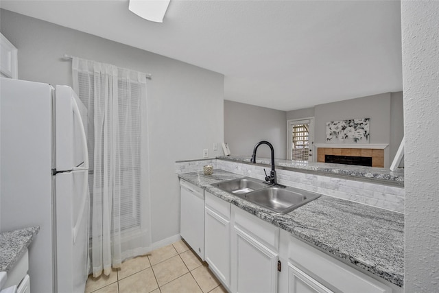 kitchen with light tile patterned floors, light stone counters, white cabinets, white appliances, and a sink