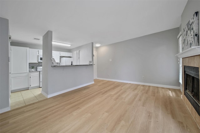 unfurnished living room with baseboards, light wood-style flooring, and a tile fireplace