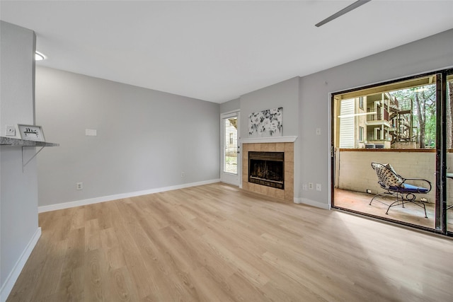 unfurnished living room with a tile fireplace, light wood-type flooring, and baseboards