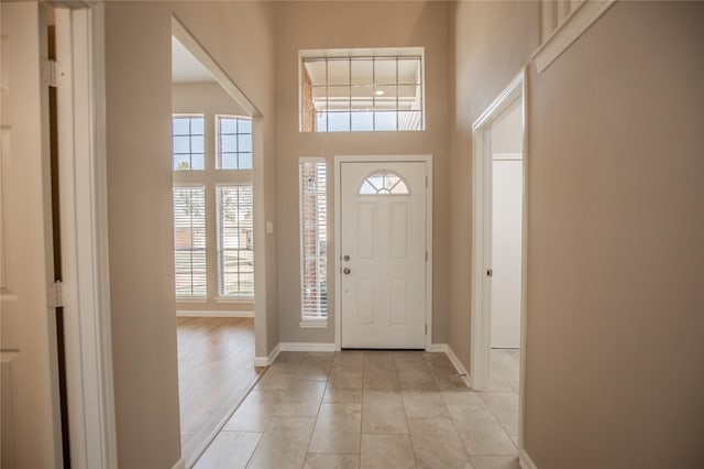 foyer entrance featuring light tile patterned flooring, baseboards, and a towering ceiling